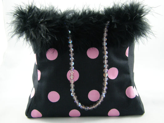 Black and Pink Evening Bag from Jenny Jag-Wear Design. This compact evening bag can be held in the palm of your hand. Black with bubble gum pink polka dots and feather trim along the top. Handcrafted glass beaded handle. The Merle Collection from Jenny Jag-Wear Design.