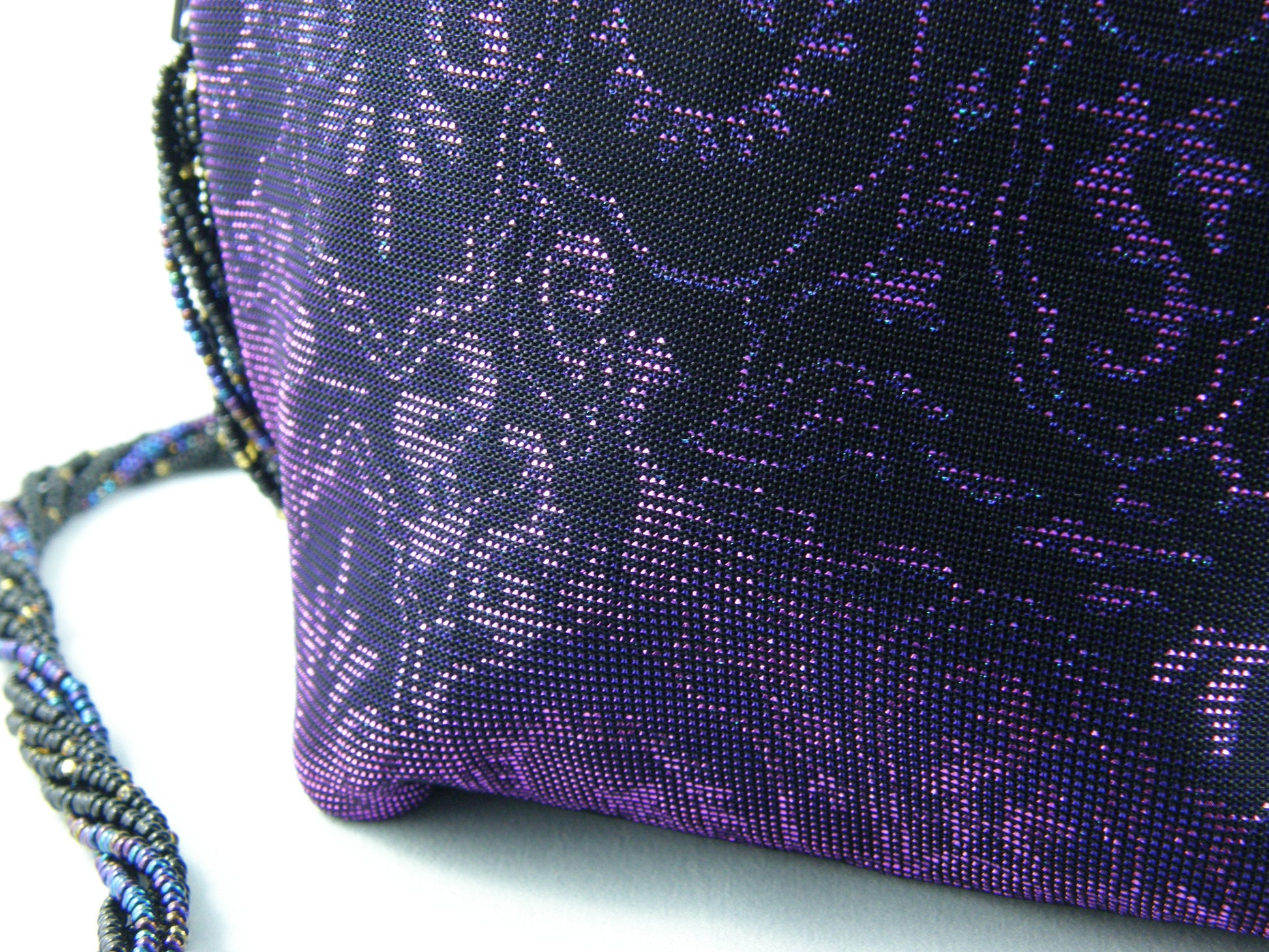 Iridescent Evening Bag from Jenny Jag-Wear Design. Image shows a close up to the iridescent fabric in hues of purple, black, and turquoise. Depending on what fabric clothing you wear, the purse fabric will off-set the outfit. If you wear black, pink, green, blue or purple, the  colour of the purse will look different based on the fabric it will complement. The Liza Collection by Jenny Jag-Wear Design.