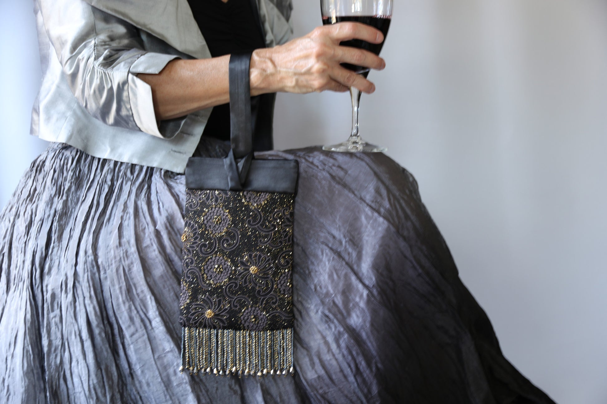 Black and Gold Evening Bag from Jenny Jag-Wear Design.  The photo shows the functionality of this compact evening bag. The model is wearing the purse on her wrist and holding a glass of wine in the same hand. The Zara Collection from Jenny Jag-Wear Design. 