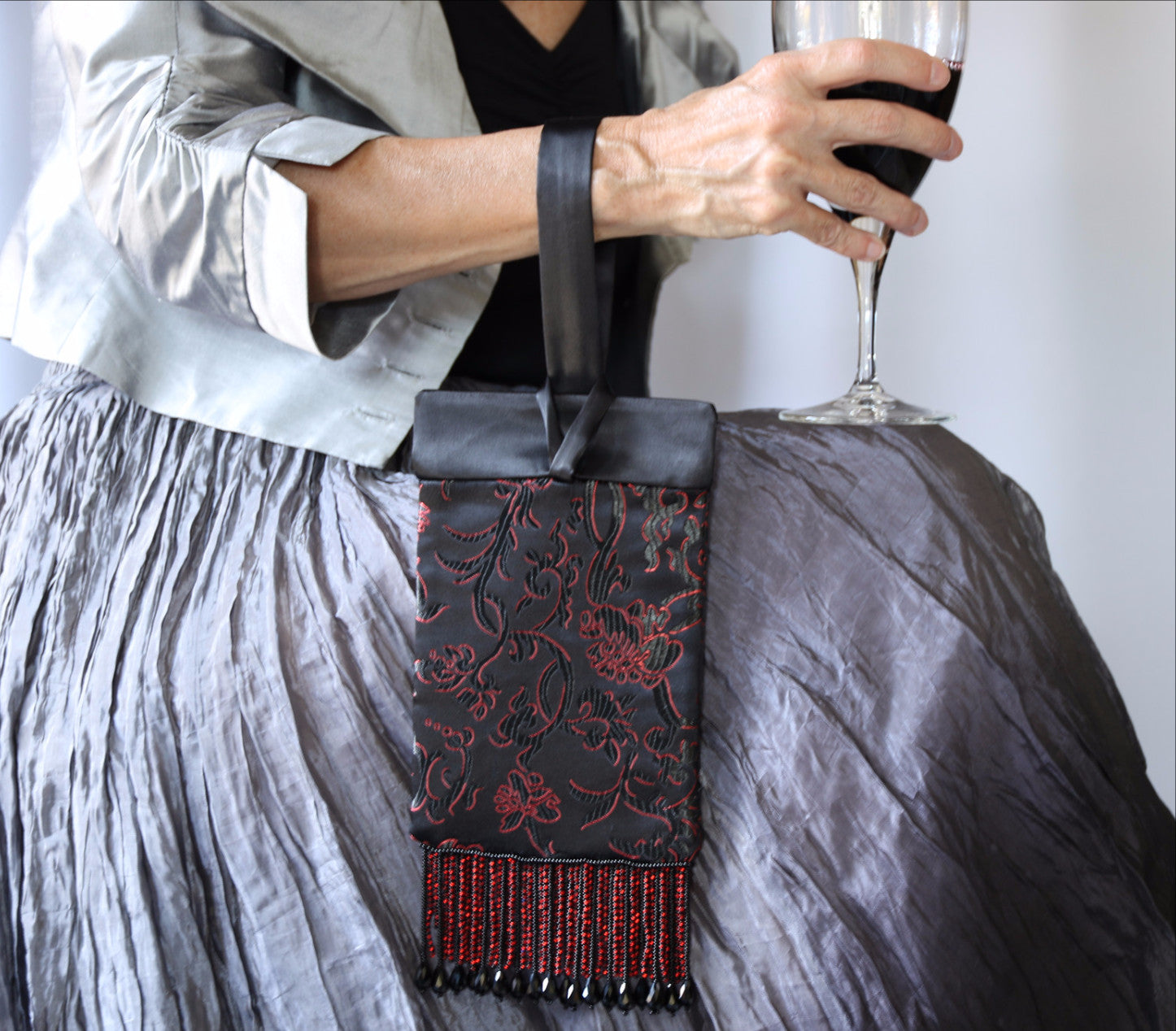 Black and Red Evening Bag from Jenny Jag-Wear Design. Photo shows the functionality of this compact evening bag. The model is wearing the purse on her wrist and holding a glass of wine in the same hand. The Zara Collection from Jenny Jag-Wear Design.